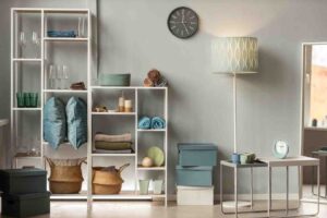 A stylish, organized living space featuring a shelving unit with glassware, towels, and decor, complemented by a floor lamp and clock.