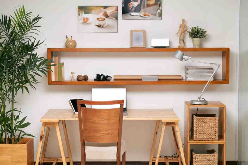A cozy home office with a wooden desk, chair, plant, and shelves displaying decor, books, and tech accessories. Soft, modern lighting.