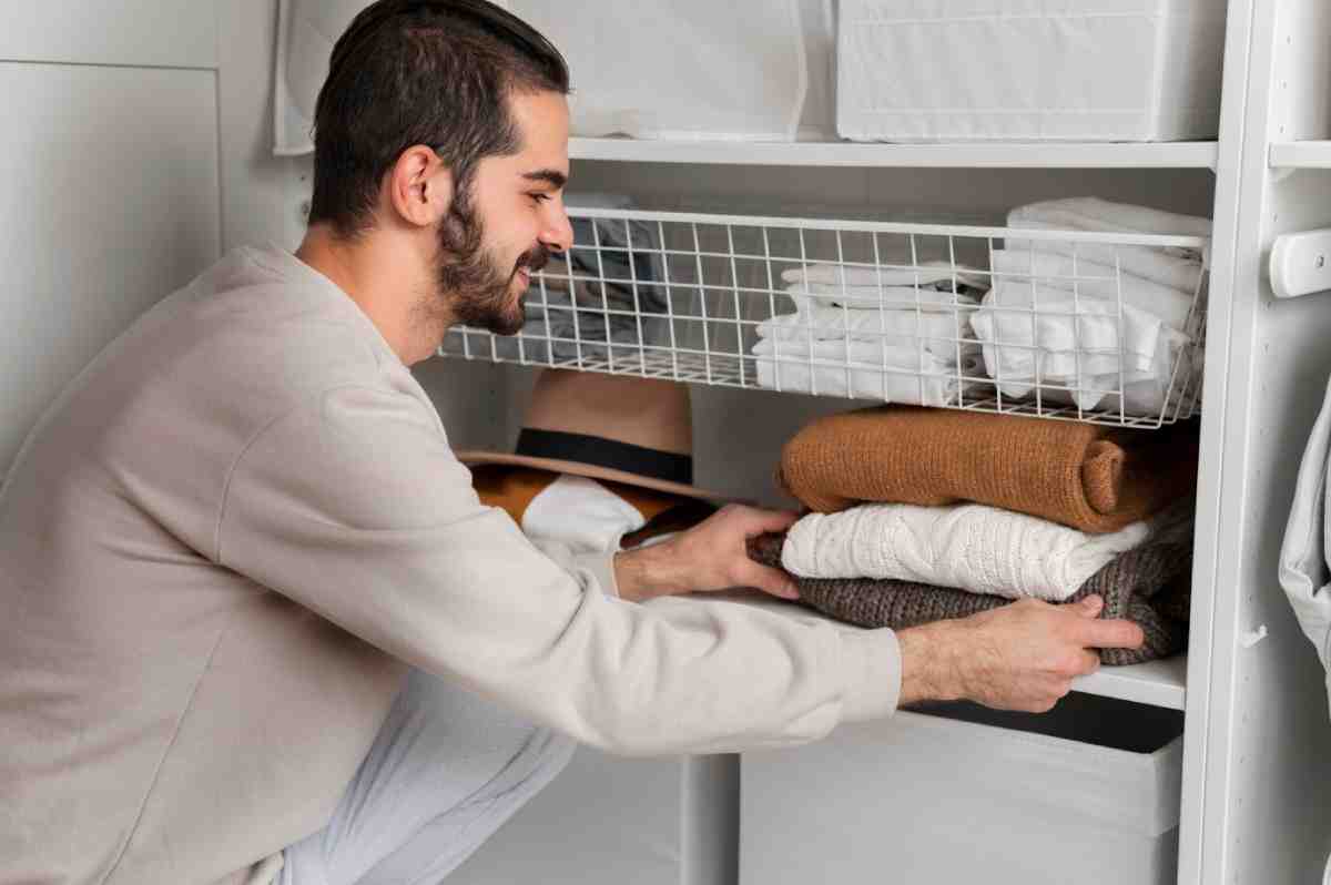 A person organizes folded sweaters and towels on a shelf in a closet, focusing on neat storage and arrangement.