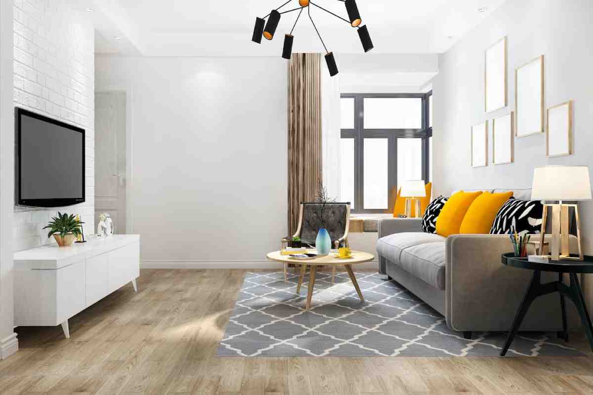 A modern living room featuring a gray sofa with yellow cushions, a round coffee table, and a TV on a white wall, filled with natural light.