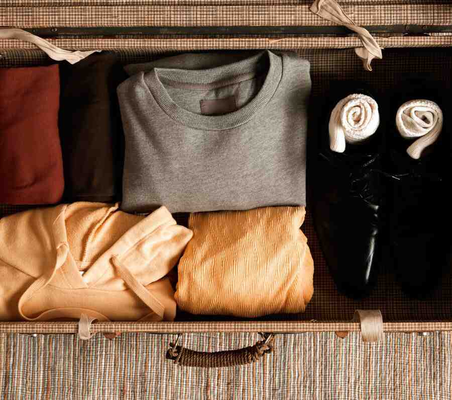 A neatly packed suitcase with folded clothing, including sweatshirts and a hoodie, beside rolled socks and polished black shoes.