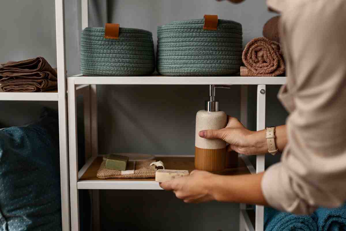 A person organizing a shelf with a soap dispenser and woven baskets, surrounded by neatly folded towels and sponges.