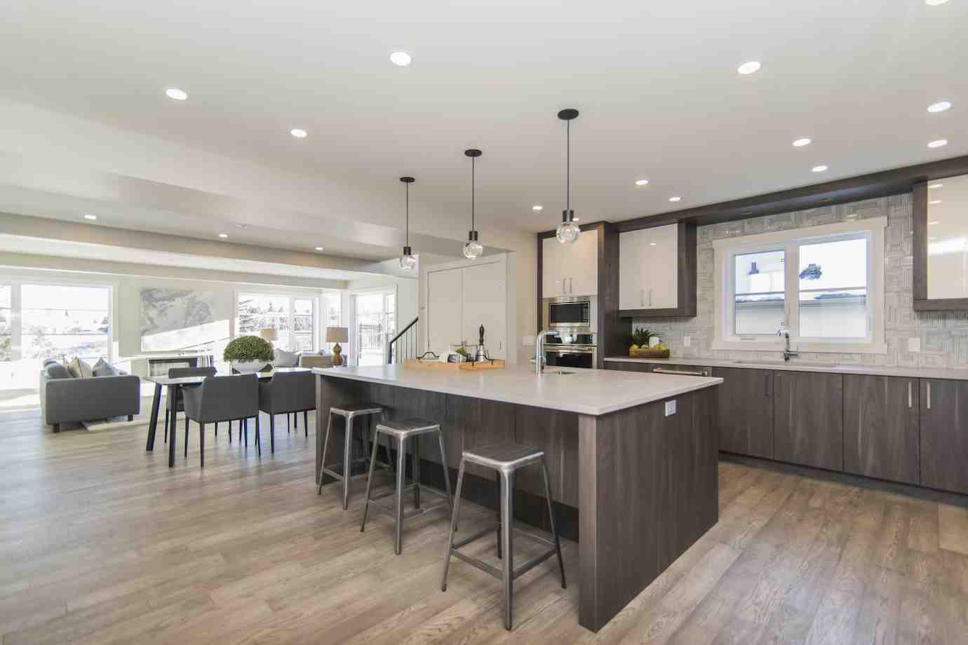Modern kitchen with a large island, bar stools, sleek cabinetry, and an open layout leading to a bright dining area. Natural light floods in.