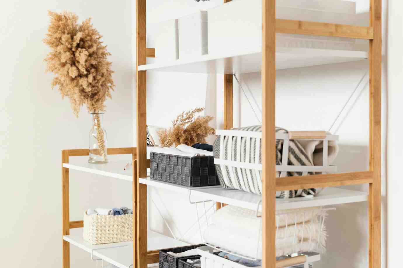A stylish wooden shelf displays decorative vases, woven baskets, and neatly folded linens in an organized, minimalist setting.