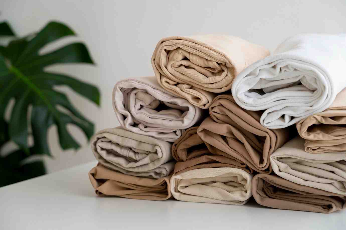 A neatly stacked arrangement of rolled fabric in various neutral shades, including cream, beige, and light brown, against a simple background.