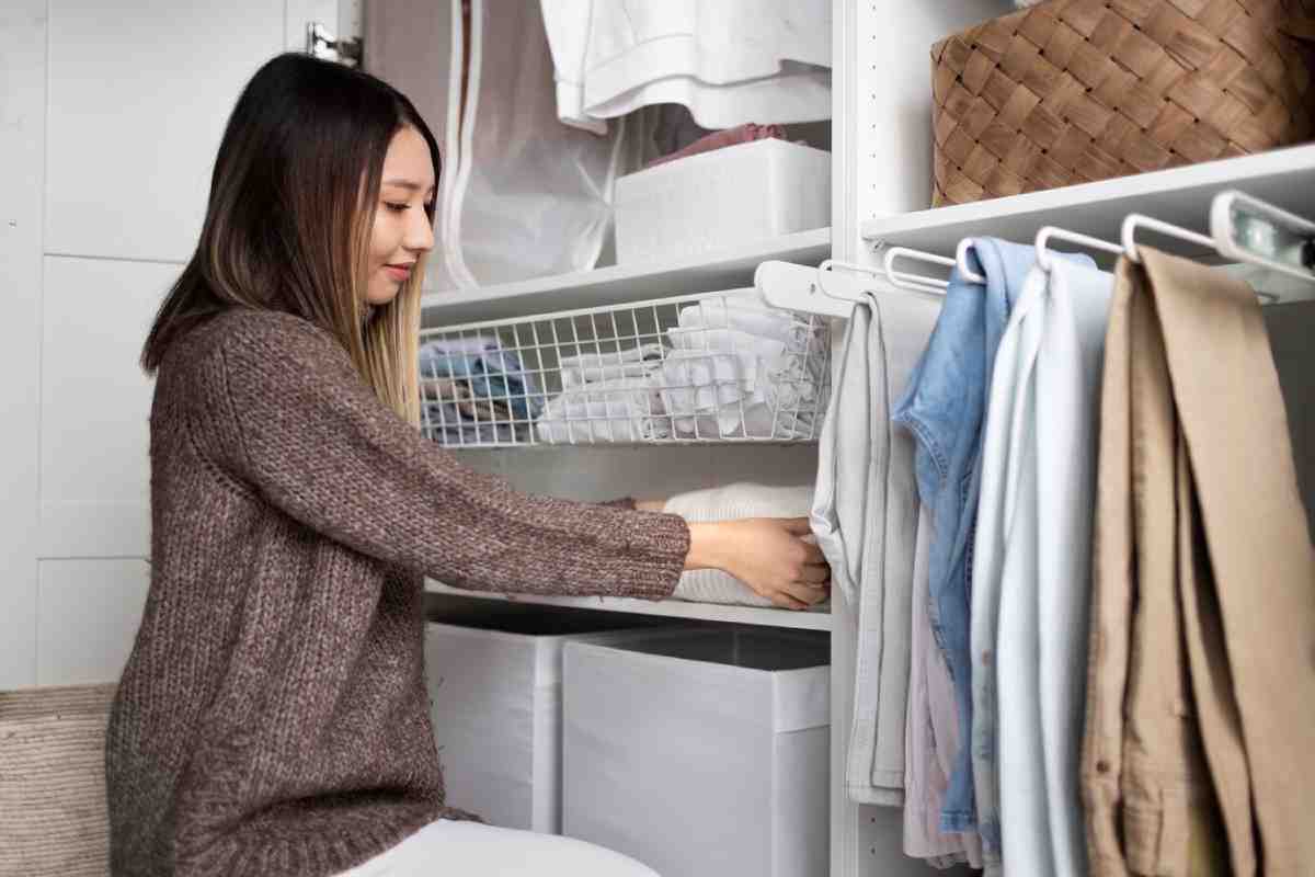 A person organizes clothes in a stylish closet, folding items and placing them in bins and shelves for efficient storage.