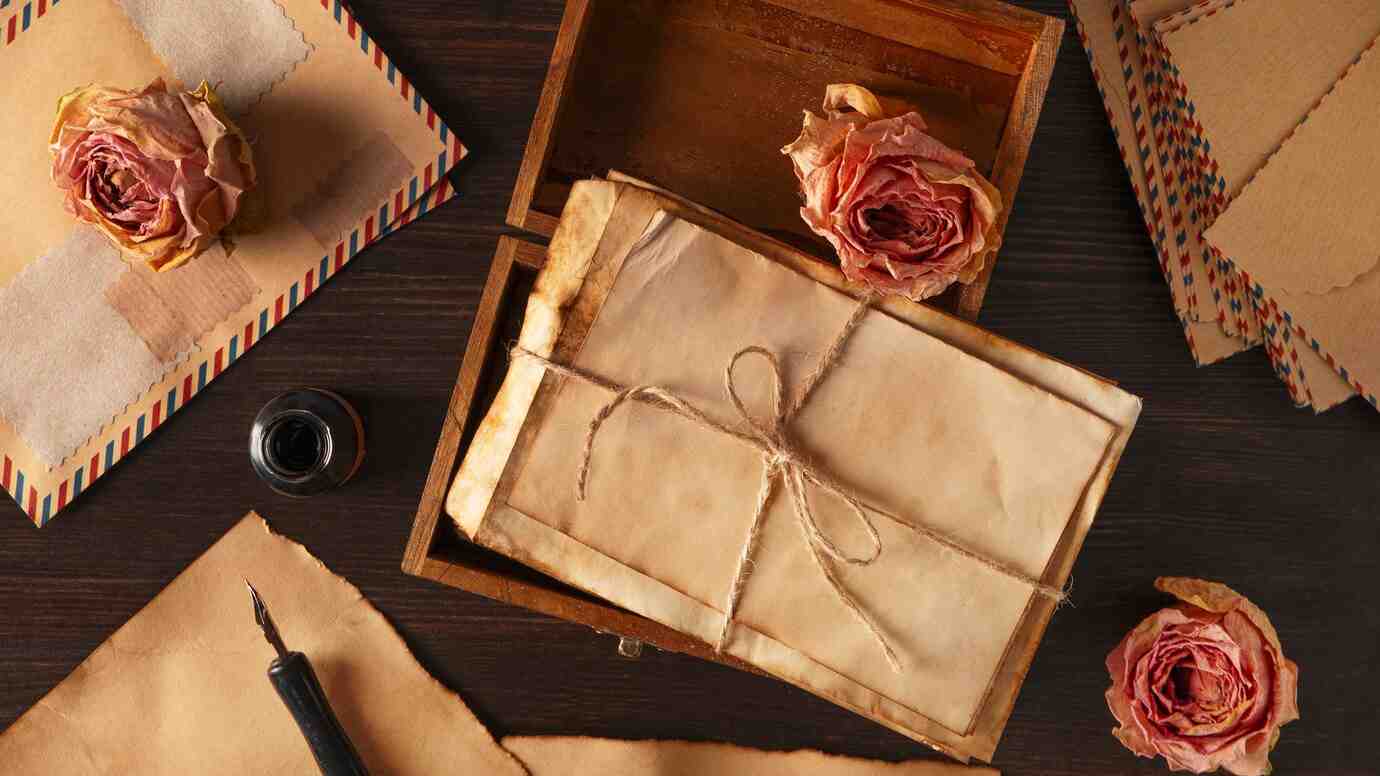 Vintage letters tied with twine, a bottle of ink, and dried roses on a dark wooden surface, evoking nostalgia and romance.