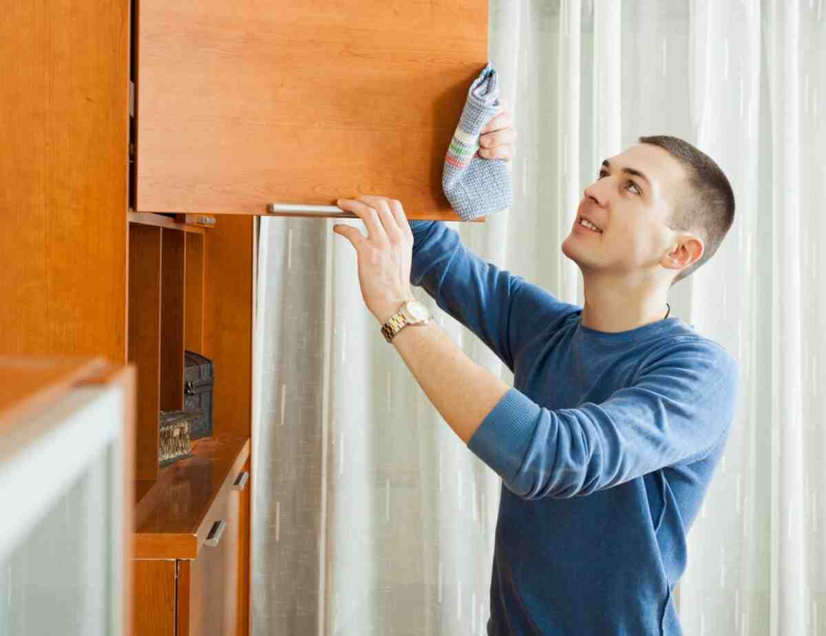 A person reaches up to open a wooden cabinet door, holding a colorful sock in one hand, indoors with sheer curtains in the background.